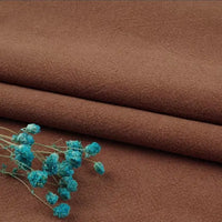 A close-up of Longan Craft’s Multiple Colors Linen Fabric By The Yard, a durable washed cotton linen blend for apparel, shown folded with a small bunch of dried blue flowers placed on top.