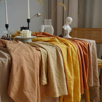 Longan Craft’s Multiple Colors Linen Fabric By The Yard in beige, yellow, and orange drapes over a table near candles, a vase with dried plants, and a white bust for a warm, artistic setting.