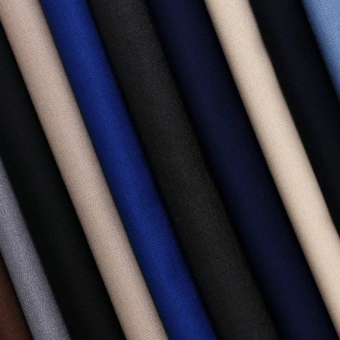 Several rolls of Longan Craft Solid Color Wool Gabardine Fabric, a rayon-polyester blended twill in beige, black, blue, and gray shades, are arranged diagonally. Ideal for casual wear.