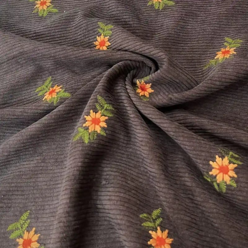 Longan Craft’s Thick 8 Wale Polyester Corduroy Fabric By The Yard features embroidered yellow, orange, and green floral accents on premium corduroy—ideal for fall apparel and upholstery projects with its distinctive swirl pattern.