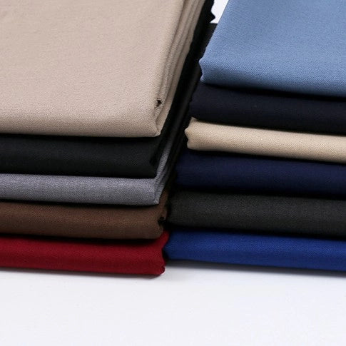 A stack of Longan Craft Solid Color Wool Gabardine Fabric by the yard, including beige, black, gray, brown, red, blue, and navy rayon polyester blended twill gabardine material for casual wear, neatly arranged on a white surface.