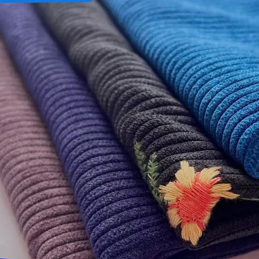 Three thick 8 wale polyester corduroy fabrics from Longan Craft—purple, dark gray with orange floral embroidery, and bright blue—are stacked side by side.