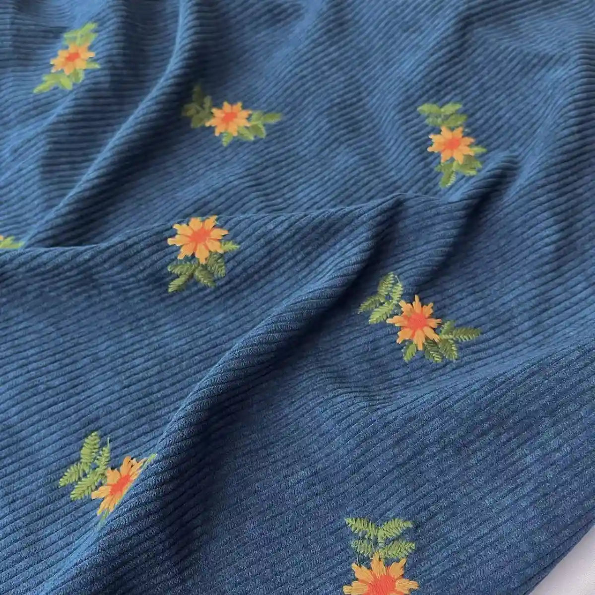 Longan Craft Thick 8 Wale Polyester Corduroy Fabric by the yard features floral embroidery in orange, yellow, and green—ideal for unique upholstery or fall apparel.
