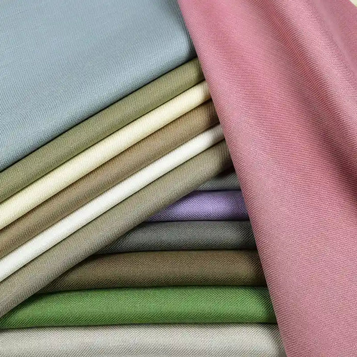 A stack of pastel pink, green, beige, gray, and lavender Longan Craft Colorful Twill 100 Lyocell fabric swatches showcases this smooth, slightly shiny sustainable material—perfect for comfortable suits.