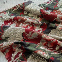 A close-up of Longan Craft’s Peony Embossed Metallic Brocade Fabric By The Yard shows luxury golden black floral jacquard texture, loosely draped with newspaper beneath, perfect for formal dresses.