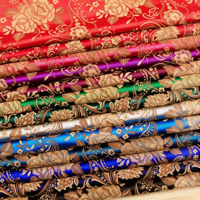 A stack of Longan Craft’s Peony Jacquard Brocade Fabric By The Yard, a colorful Chinese floral brocade with gold accents in red, purple, green, blue, and white—ideal material for formal dresses—neatly arranged in a pile.