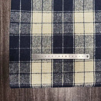 A metal ruler lies horizontally across Longan Craft's Plaid Brushed Mammoth Flannel Fabric By The Yard, a colorful polyester cotton material, displayed on a wood-textured surface. The ruler measures about 16 centimeters long.