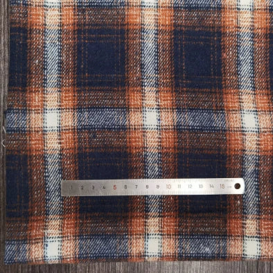 The Longan Craft Plaid Brushed Mammoth Flannel Fabric by the yard, a blue, orange, and white polyester-cotton blend, is displayed on wood with a metal ruler showing about 15 cm across the comfy fall flannel surface.
