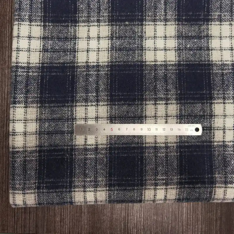 A metal ruler rests on a Longan Craft Plaid Brushed Mammoth Flannel Fabric by the yard, featuring colorful polyester-cotton flannel, with the fabric laid on a wooden surface.