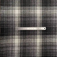 A silver 15 cm ruler lies horizontally on Longan Craft's Plaid Brushed Mammoth Flannel by the yard—a soft, colorful polyester-cotton fabric with a black, white, and gray checkered pattern.