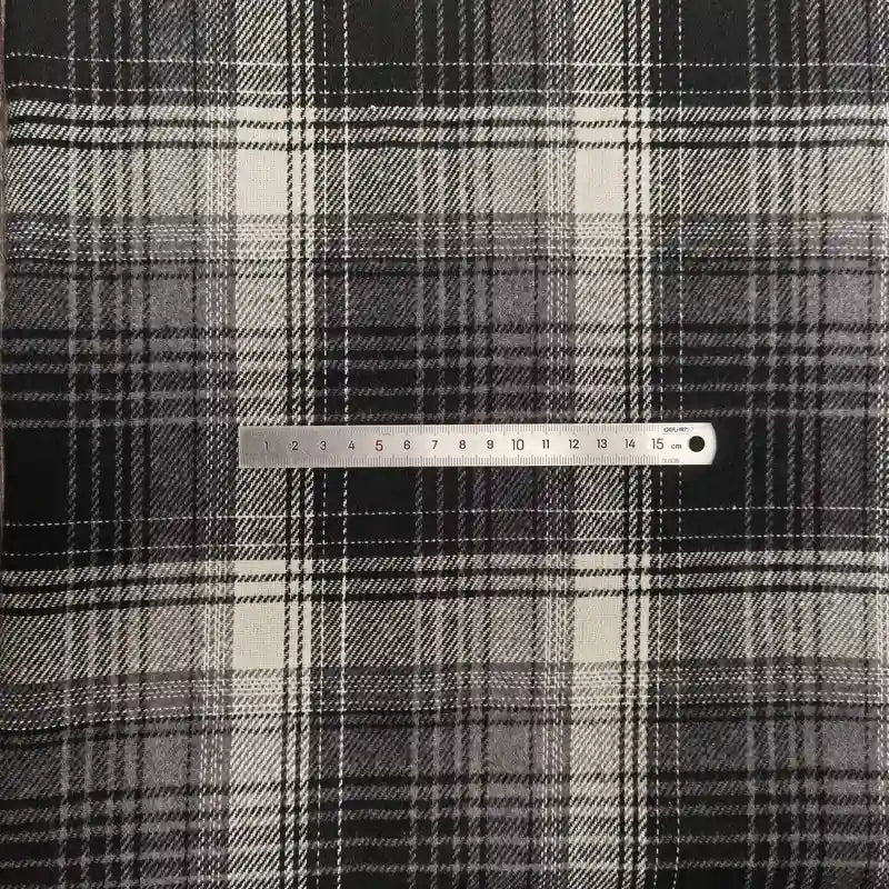 A silver 15 cm ruler lies horizontally on Longan Craft's Plaid Brushed Mammoth Flannel by the yard—a soft, colorful polyester-cotton fabric with a black, white, and gray checkered pattern.