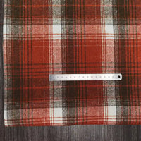 A silver ruler rests on Longan Craft's Plaid Brushed Mammoth Flannel Fabric By The Yard, a colorful polyester cotton material, with its scale visible against the comfy fall plaid pattern atop a dark wood surface.