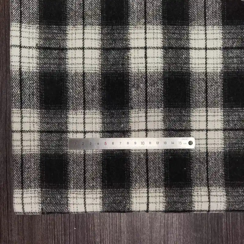 A Longan Craft Plaid Brushed Mammoth Flannel Fabric lies under a metal ruler on a dark wood surface, displaying the pattern scale. This comfy polyester cotton flannel is perfect for fall projects and is sold by the yard.