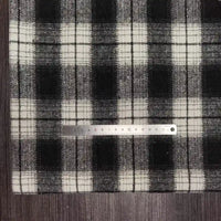 A Longan Craft Plaid Brushed Mammoth Flannel Fabric lies under a metal ruler on a dark wood surface, displaying the pattern scale. This comfy polyester cotton flannel is perfect for fall projects and is sold by the yard.