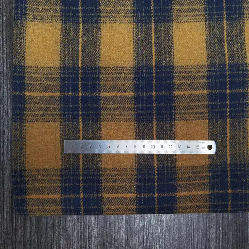 A silver 15cm ruler rests on Longan Craft’s Plaid Brushed Mammoth Flannel Fabric, a colorful polyester-cotton material, displayed atop a dark wooden surface.