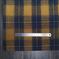 A silver 15cm ruler rests on Longan Craft’s Plaid Brushed Mammoth Flannel Fabric, a colorful polyester-cotton material, displayed atop a dark wooden surface.