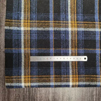 A piece of Longan Craft Plaid Brushed Mammoth Flannel Fabric By The Yard, a colorful polyester cotton material with blue, yellow, white, and black stripes, lies on wood with a metal centimeter ruler across its soft surface.