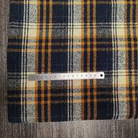 A metal ruler lies on top of Longan Craft's Plaid Brushed Mammoth Flannel Fabric By The Yard—colorful polyester cotton plaid flannel—resting on a grey textured surface. Ruler shows measurements in centimeters.