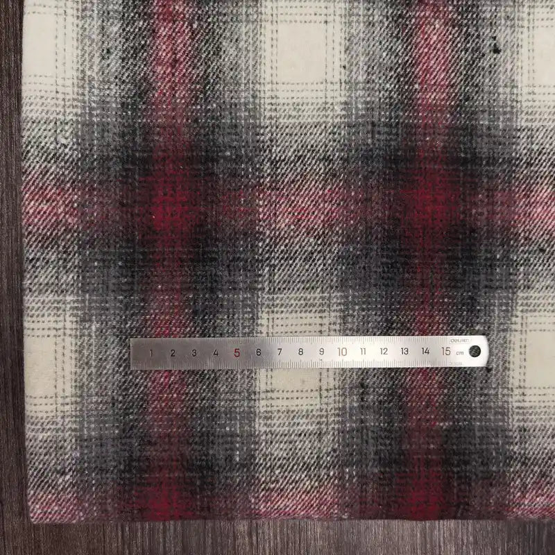 A metal ruler measuring about 15cm lies on Longan Craft's Plaid Brushed Mammoth Flannel Fabric—a colorful polyester-cotton material in black, red, and white—displayed on a wooden surface.