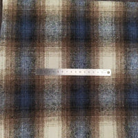 A 15cm metal ruler lies horizontally across Longan Craft's Plaid Brushed Mammoth Flannel Fabric, a comfy fall polyester-cotton material featuring a colorful brown, blue, and white plaid pattern.