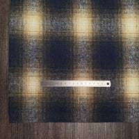 A steel ruler measures Longan Craft’s Plaid Brushed Mammoth Flannel Fabric by the yard, featuring a colorful polyester cotton pattern. The ruler lies horizontally across the comfy fall fabric on a dark wooden surface.