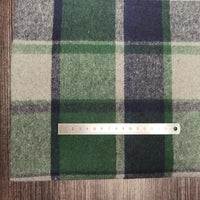 A 15cm metal ruler sits on Longan Craft’s Plaid Brushed Mammoth Flannel Fabric by the Yard—a green, navy, and beige polyester cotton material—spread out on a wooden surface.