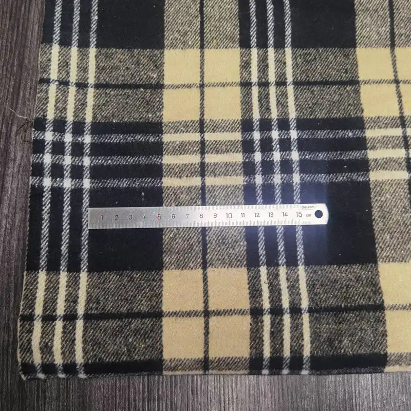 A metallic ruler measuring centimeters rests on Plaid Brushed Mammoth Flannel Fabric by Longan Craft, a colorful polyester cotton material, atop a dark wooden surface.