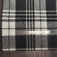 A metal ruler rests on Longan Craft's Plaid Brushed Mammoth Flannel Fabric By The Yard, a colorful polyester cotton flannel. The comfy fall fabric displays black, white, and gray plaid atop a wooden surface.