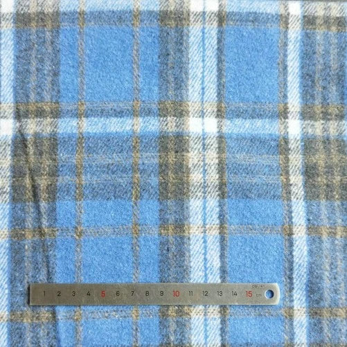 A metal ruler marked in red and black centimeters (up to 15 cm) lies on Longan Craft’s Plaid Brushed Mammoth Flannel Fabric, a colorful polyester cotton flannel sold by the yard as comfy fall material.