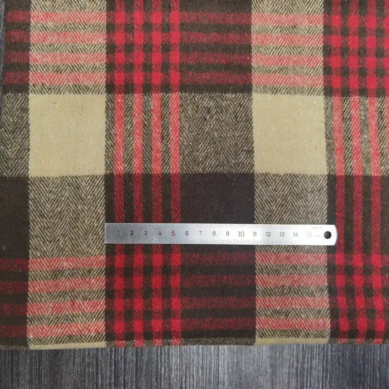 A metal ruler rests on Longan Craft’s Plaid Brushed Mammoth Flannel Fabric—a colorful polyester cotton flannel material—showing checkered red, brown, and tan patterns atop a dark wood surface. The ruler displays centimeter markings.