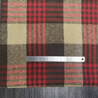 A metal ruler rests on Longan Craft’s Plaid Brushed Mammoth Flannel Fabric—a colorful polyester cotton flannel material—showing checkered red, brown, and tan patterns atop a dark wood surface. The ruler displays centimeter markings.