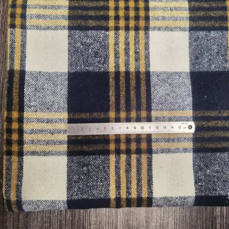 A 15-cm metal ruler rests on Longan Craft’s Plaid Brushed Mammoth Flannel Fabric by the Yard, a colorful polyester cotton material, illustrating the blue, yellow, and white plaid pattern's scale.