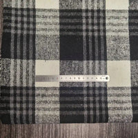 A metal ruler rests on Longan Craft’s Plaid Brushed Mammoth Flannel Fabric By The Yard, a colorful polyester cotton flannel, both set atop a wooden surface; the ruler displays centimeter markings.