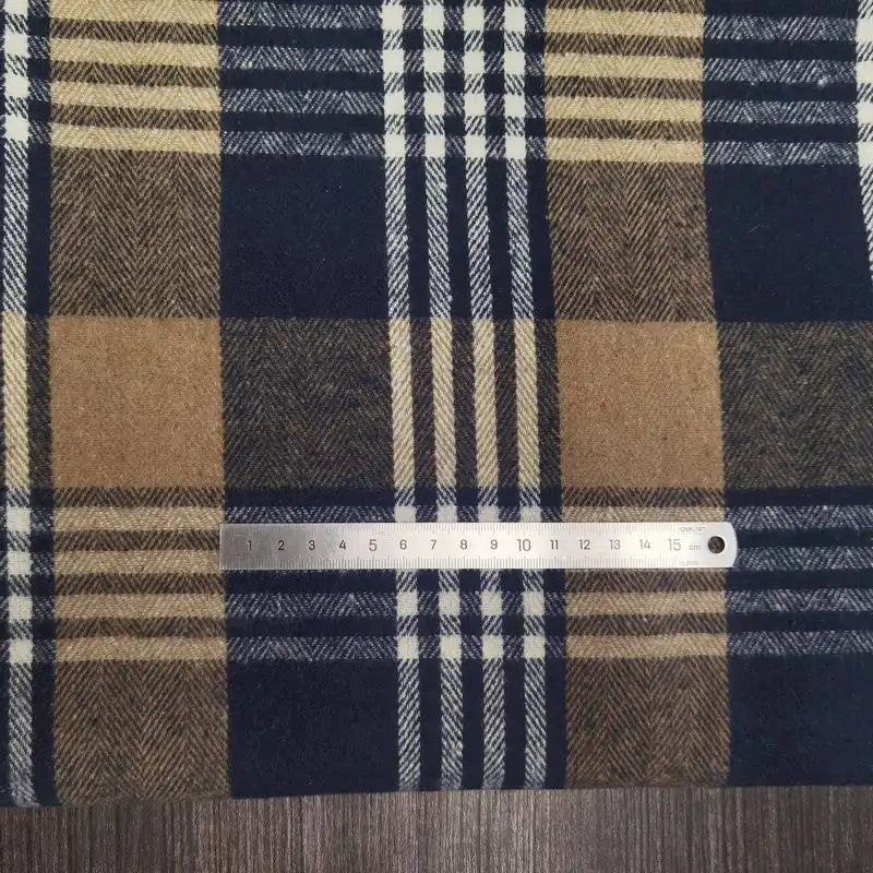 A metal ruler measures up to 15 centimeters on Longan Craft’s Plaid Brushed Mammoth Flannel Fabric by the Yard, a comfy polyester cotton material featuring a blue, tan, and cream checkered pattern.