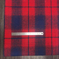 A silver ruler rests on Longan Craft Plaid Brushed Mammoth Flannel Fabric by the Yard, a comfy polyester-cotton material with large red and navy blue checks, displayed on a wood-textured surface. The ruler shows cm and mm measurements.