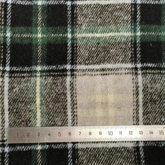A close-up of Longan Craft Plaid Brushed Mammoth Flannel Fabric by the yard shows its green, black, and white design with a silver metal ruler measuring 0–15 cm placed horizontally at the bottom.