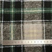 A close-up of Longan Craft Plaid Brushed Mammoth Flannel Fabric by the yard shows its green, black, and white design with a silver metal ruler measuring 0–15 cm placed horizontally at the bottom.