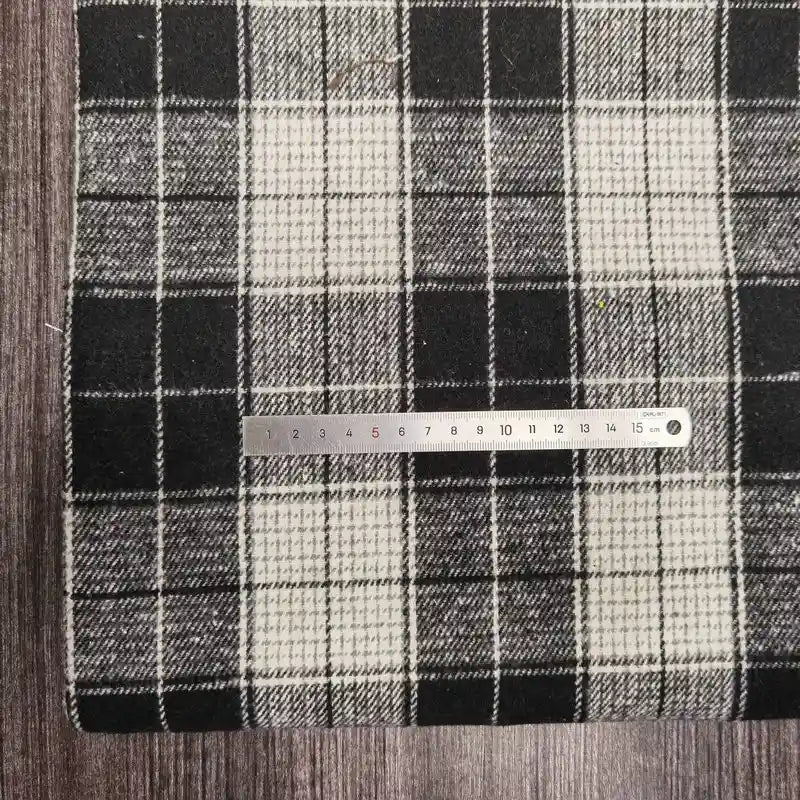 A metal ruler rests on Longan Craft’s Plaid Brushed Mammoth Flannel Fabric by the Yard, a colorful polyester-cotton material with a checkered pattern, placed atop a dark wooden surface.