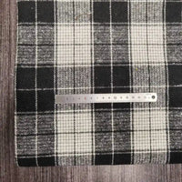 A metal ruler rests on Longan Craft’s Plaid Brushed Mammoth Flannel Fabric by the Yard, a colorful polyester-cotton material with a checkered pattern, placed atop a dark wooden surface.