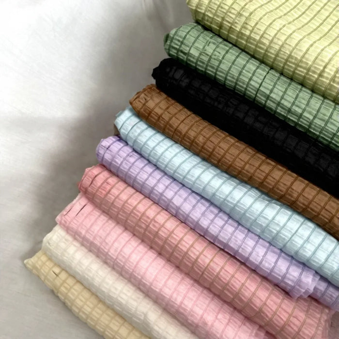 A stack of Longan Craft’s Plaid Jacquard Lyocell Fabric By The Yard, in multicolor check patterns, is neatly arranged diagonally on a white surface—showcasing this breathable, eco-friendly material for apparel.