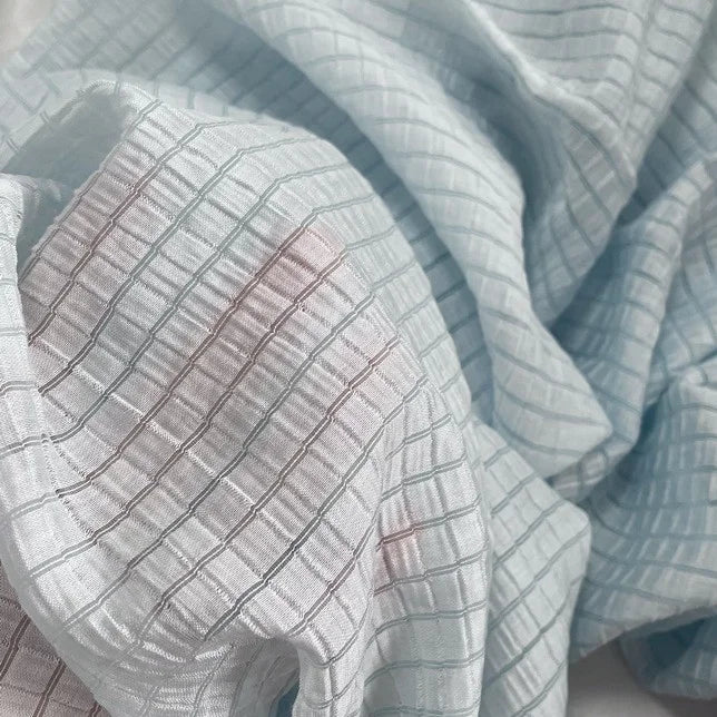 A close-up of Longan Craft's Plaid Jacquard Lyocell Fabric By The Yard reveals its soft, multicolor checked texture. This breathable, sustainable textile for apparel displays a slightly crumpled look with subtle shadows and hints of pink.