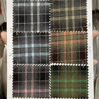 A hand holds a sheet showing six numbered swatches of Longan Craft's Plaid Mammoth Flannel Fabric By The Yard, each with unique plaid patterns on dark backgrounds. This comfy polyester rayon textile is ideal for shirting and crafts.