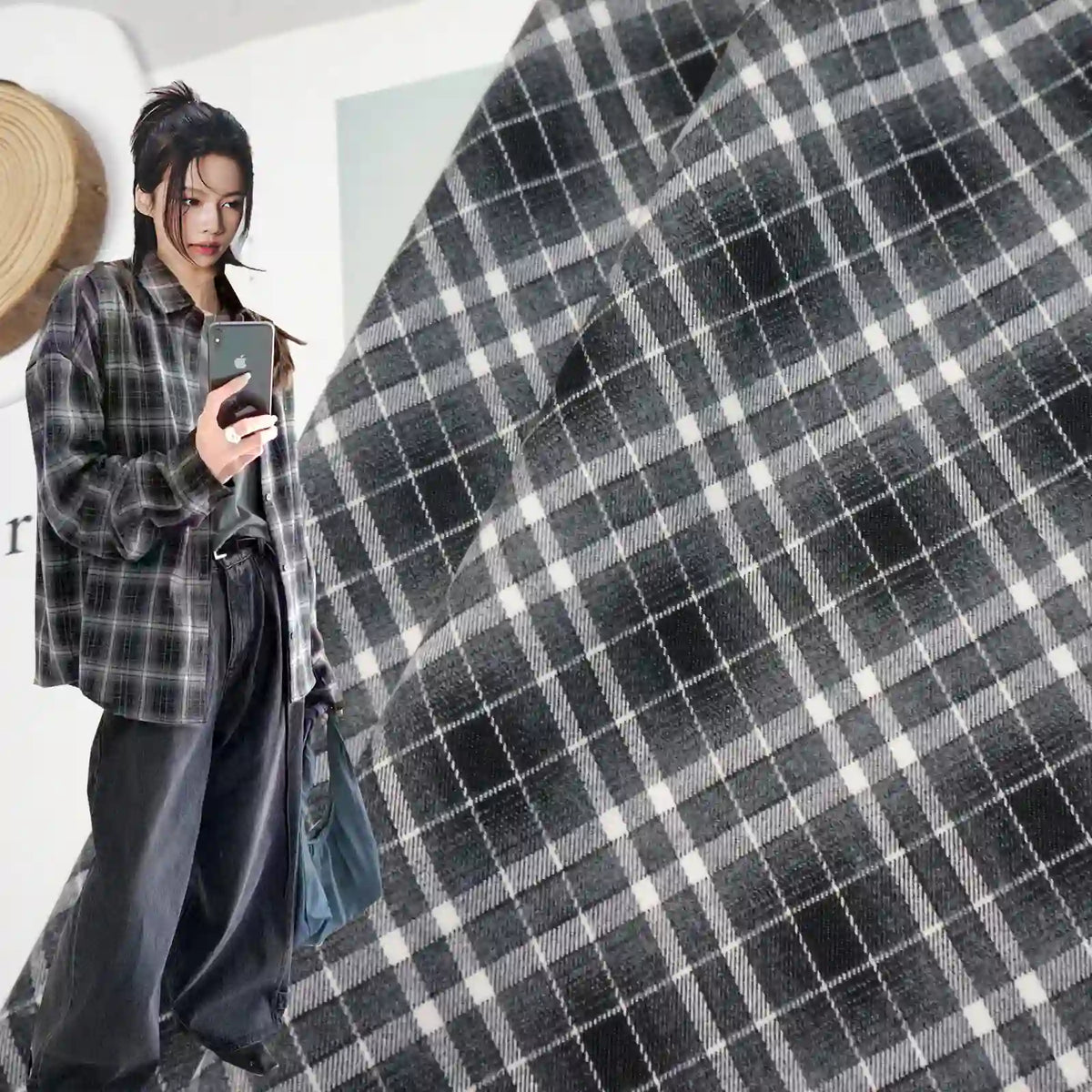 A woman wears a shirt made from Longan Craft's Plaid Mammoth Flannel Fabric By The Yard—comfy polyester rayon shirting flannel—in black and gray plaid, paired with loose black pants, taking a mirror selfie with a close-up of the same plaid pattern in the background.