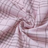 Soft plaid print 16-wale corduroy fabric by Longan Craft, shown gathered and twisted to highlight its colorful fine wale texture and subtle grid pattern in brown on a light pink background. The clear corduroy lines make this premium fabric ideal for pants and creative sewing projects.
