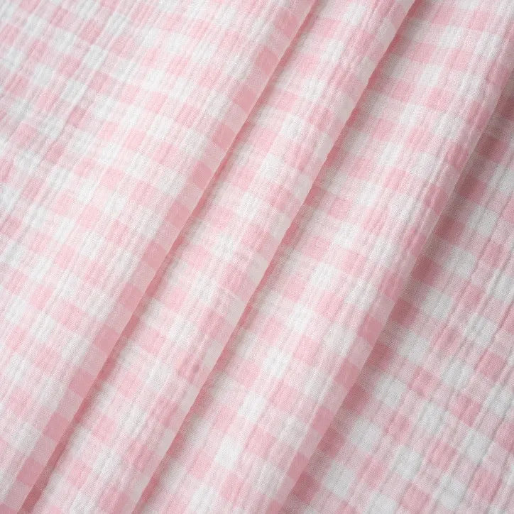 Close-up of Plaid Print Double Gauze Fabric By The Yard from Longan Craft, featuring a pink and white gingham checkered pattern in pure cotton. This cozy gauze material displays soft folds and a textured surface, making it a breathable and comfortable choice for baby clothing and stylish sewing projects.