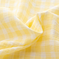 Close-up view of the Plaid Print Double Gauze Fabric by Longan Craft, featuring a yellow and white checkered pattern with a soft, crinkled texture. The gentle folds emphasize the light and airy quality of this pure cotton checked gauze material, making it a cozy, breathable choice—perfect for creating comfortable baby clothing and other garments.