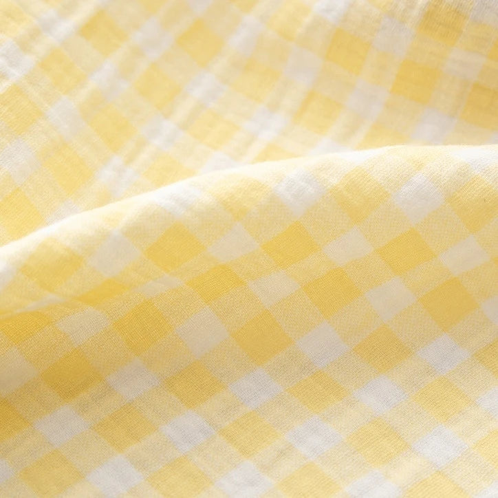Close-up of the Plaid Print Double Gauze Fabric By The Yard from Longan Craft, featuring a yellow and white checked pattern on pure cotton gauze material. The soft folds and airy texture highlight the fabric’s breathable qualities, making it ideal for cozy baby clothing.
