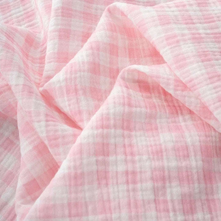 Light pink and white checkered fabric with a soft, crinkled texture, shown in gentle folds and creases—Longan Craft’s Plaid Print Double Gauze Fabric By The Yard is a breathable pure cotton gauze, perfect for cozy baby clothing and stylish projects.