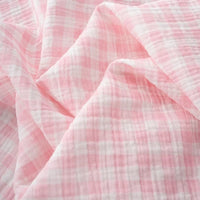 Light pink and white checkered fabric with a soft, crinkled texture, shown in gentle folds and creases—Longan Craft’s Plaid Print Double Gauze Fabric By The Yard is a breathable pure cotton gauze, perfect for cozy baby clothing and stylish projects.