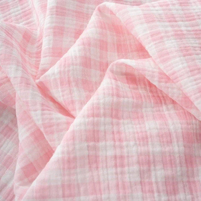 Light pink and white checkered fabric with a soft, crinkled texture, shown in gentle folds and creases—Longan Craft’s Plaid Print Double Gauze Fabric By The Yard is a breathable pure cotton gauze, perfect for cozy baby clothing and stylish projects.